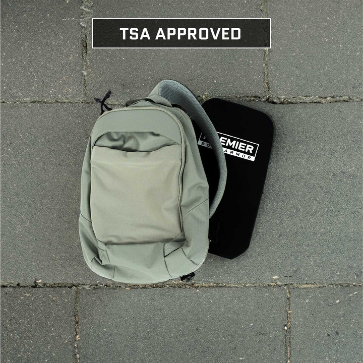 A gray backpack sits on a tiled surface, alongside a black rectangular object with "Premier Body Armor" prominently displayed. The Vertx Ghost Sling Level IIIA/HG2 Backpack Insert boasts Level IIIA protection and proudly features a "TSA APPROVED" sign.