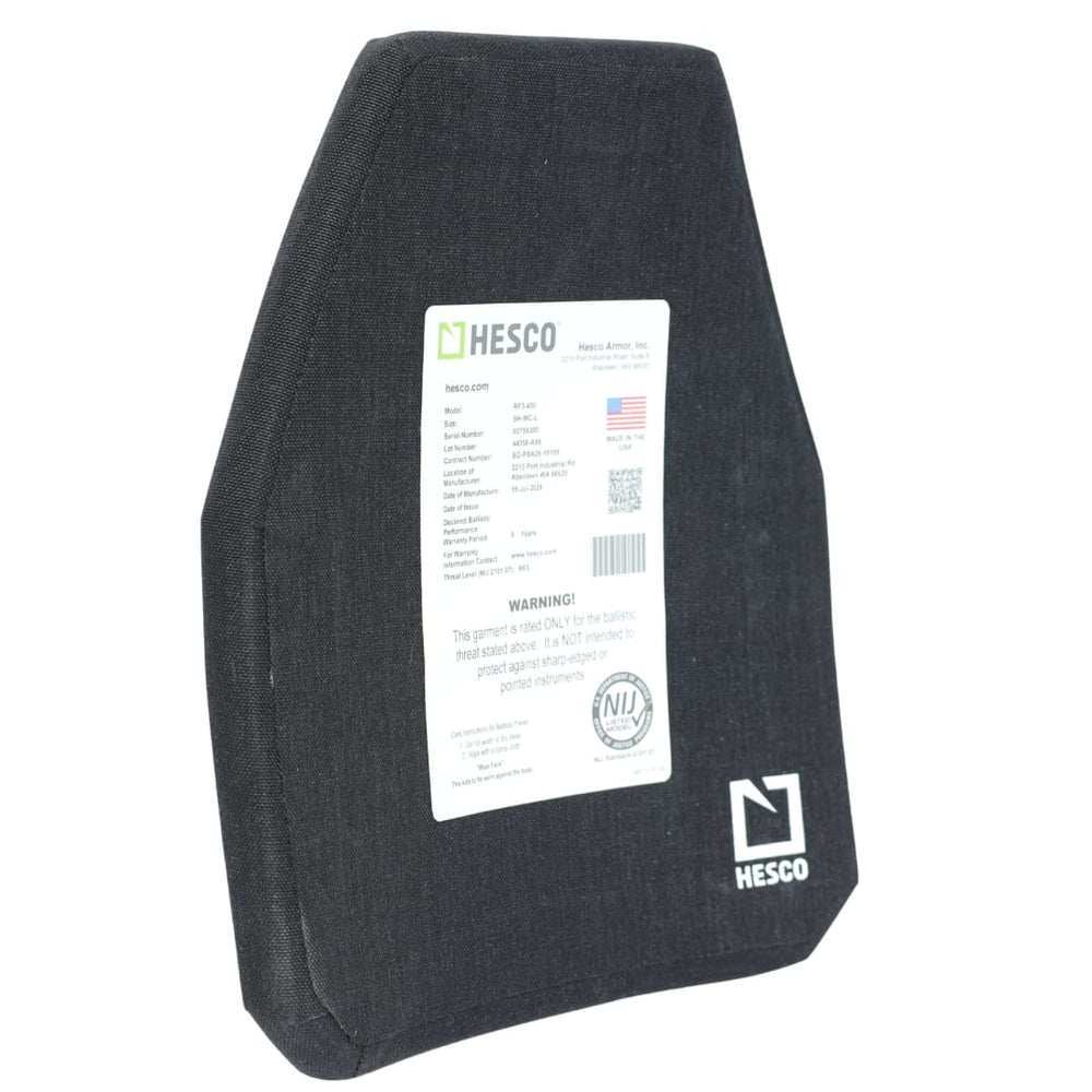 A black Hesco RF3-400 ballistic armor plate stands upright. A white label with specifications and a warning is attached to the center. Designed as a HESCO RF3-400, this ceramic/composite armor offers light AP protection for enhanced safety. The Hesco logo is visible in the bottom right corner.