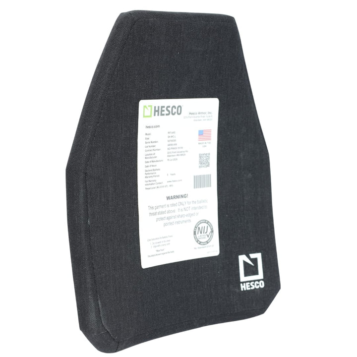 A black Hesco RF3-400 ballistic armor plate stands upright. A white label with specifications and a warning is attached to the center. Designed as a HESCO RF3-400, this ceramic/composite armor offers light AP protection for enhanced safety. The Hesco logo is visible in the bottom right corner.