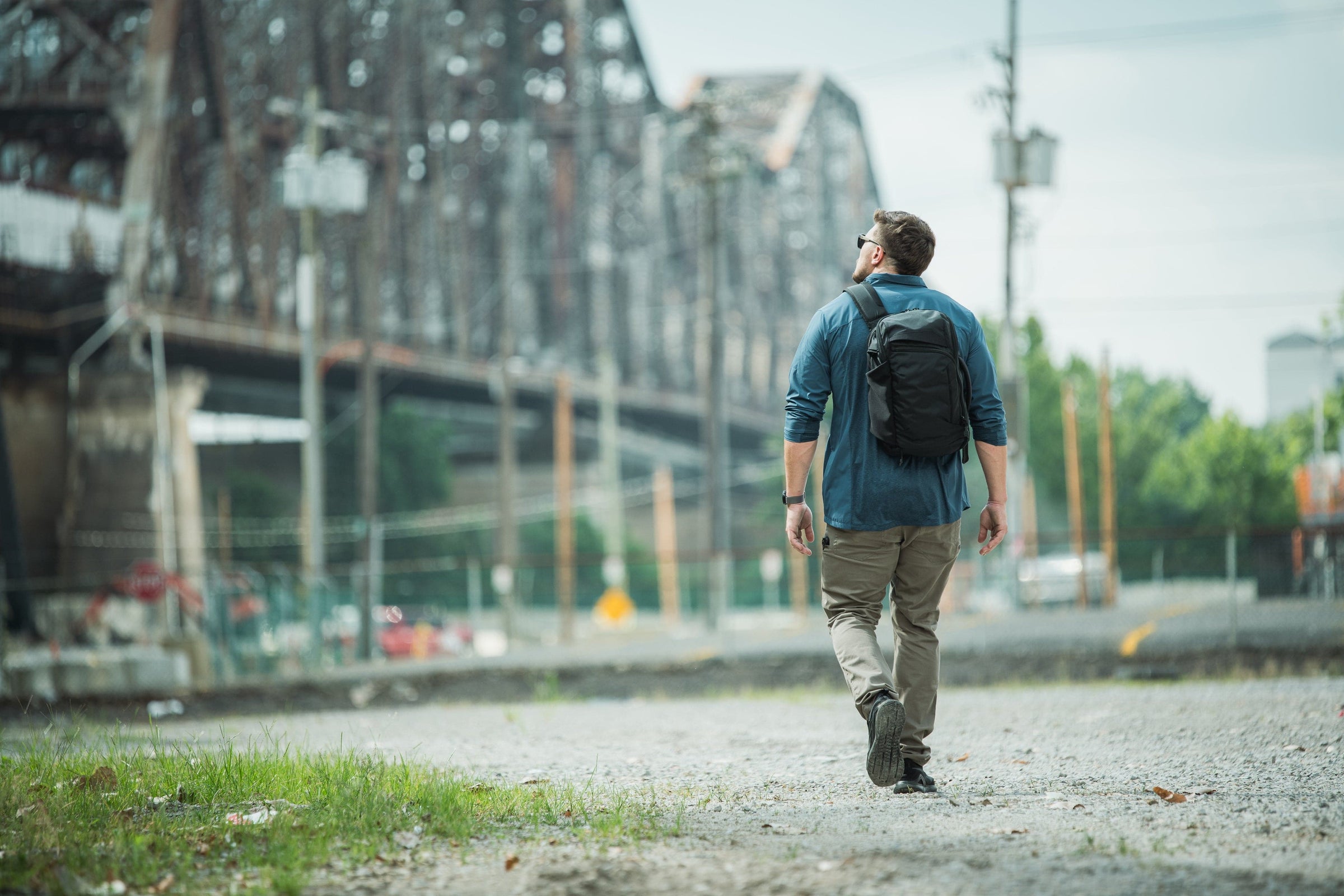 Man walking with a backpack on a path near industrial structures
