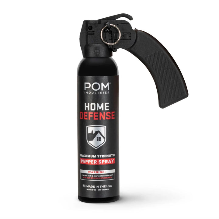 The POM Home Defense Pepper Spray by POM is a black canister with a large pistol-grip handle and trigger, includes a warning label, and is made in the USA.