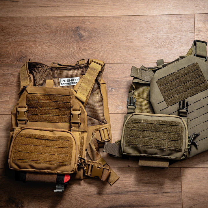 A tan and a green tactical plate carrier from Premier Body Armor, each with front pouches, multiple Velcro strips, and a Fortis Pro Placard (556/39) AR-15 magazine holder with Kydex retention, are displayed on a wooden floor.