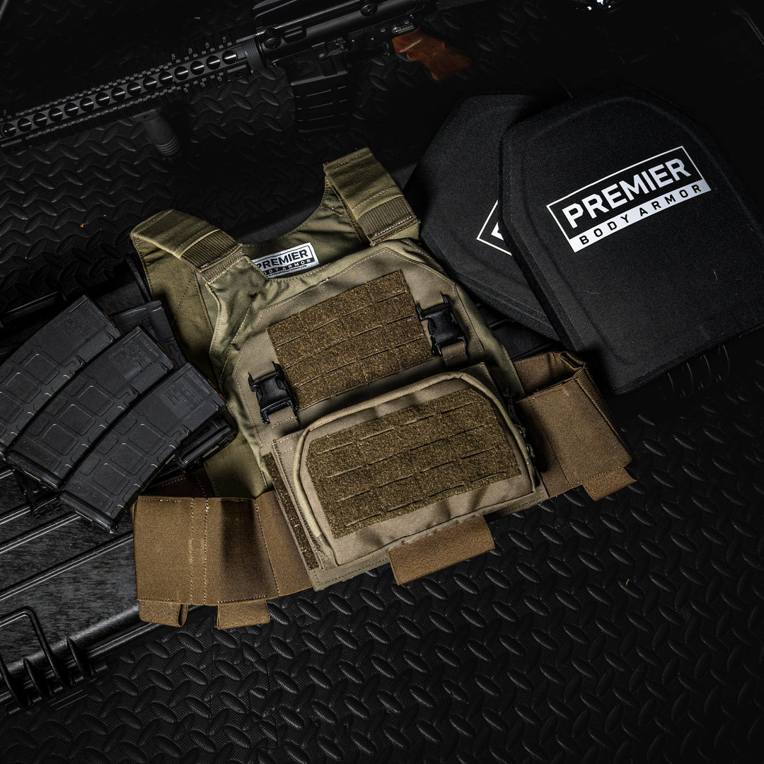 A Fortis Bravo Low Profile Carrier by Premier Body Armor, equipped with velcro pouches, two black body armor plates labeled “Premier Body Armor,” laser cut MOLLE attachments, three rifle magazines, and a firearm are arranged on a textured black surface.