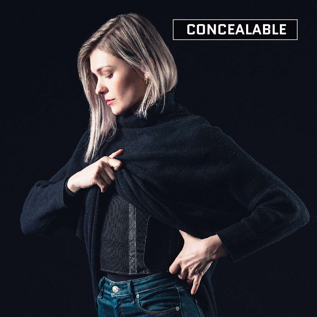 A person with light hair is pulling their dark sweater aside, revealing a Premier Body Armor Female Concealable Armor Vest - Level IIIA underneath. The word "CONCEALABLE" is written in bold letters at the top right corner of the image. The background is dark.