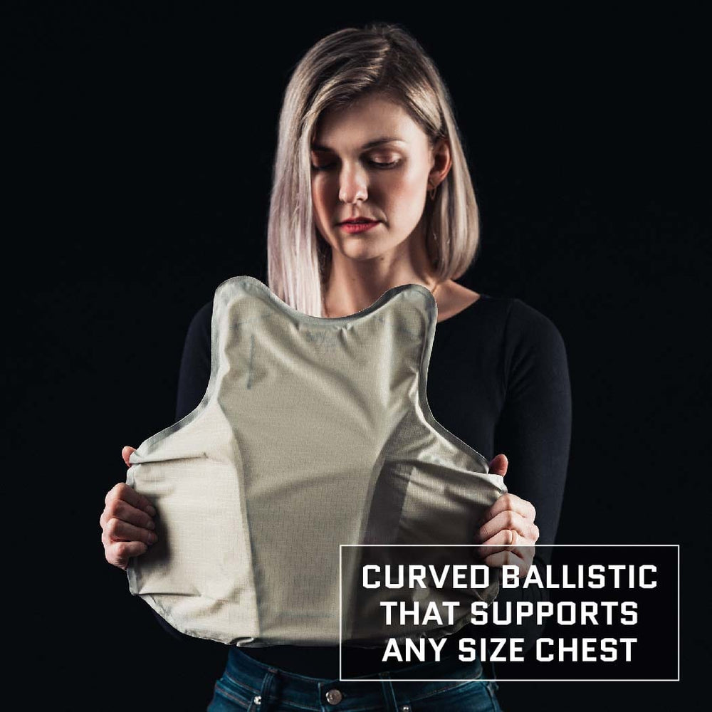 A person with long blonde hair is holding a Female Concealable Armor Vest - Level IIIA. The background is black, and text on the image reads, "Curved ballistic that supports any size chest." The person, wearing a black long-sleeve top and blue jeans, showcases our Premier Body Armor's vest designed for women.