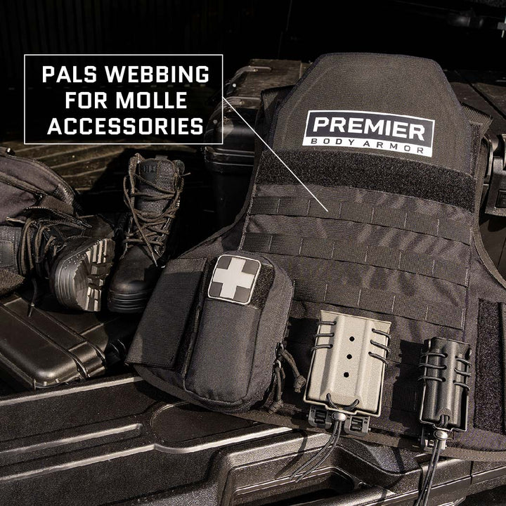 A black Premier Body Armor Overt / Covert Vest Bundle with PALS webbing for MOLLE accessories is displayed. It includes a medical pouch marked with a white cross symbol. Tactical boots and other equipment are also visible in the background.