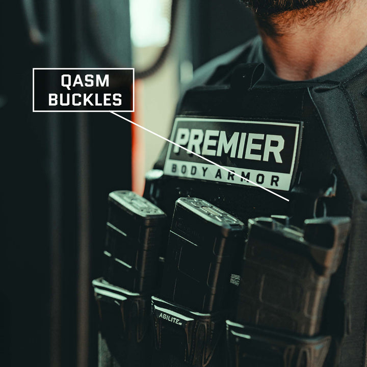 Close-up of a person wearing the Premier Body Armor Fortis Level IV Loadout vest, featuring labeled QASM buckles. The Fortis Alpha Carrier part of the vest includes multiple magazine pouches filled with magazines, offering tactical flexibility. The person's face is not visible in the image.