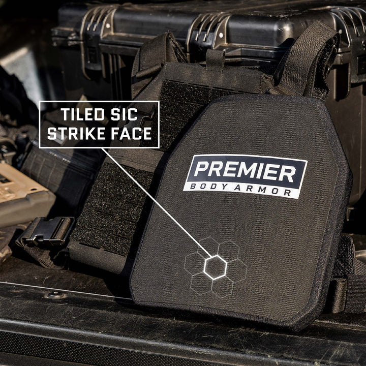 The Fortis III+ GT/RF2 Single-Curve body armor plate from Premier Body Armor, featuring a highlighted "Tiled SiC Strike Face," is set on black tactical equipment including a case and vests in the back of a vehicle. This Level III+ ballistic plate integrates Boron/Silicon Carbide tiles for superior protection.