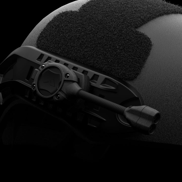 Close-up of a black tactical helmet showcasing a textured surface, designed for Tactical Professionals. It features a mount with an attached flexible arm that ends in dual circular components compatible with the Princeton Tec Switch RGB MPLS Helmet Light. A Velcro patch is visible on top, and the dark background accentuates the helmet's details.