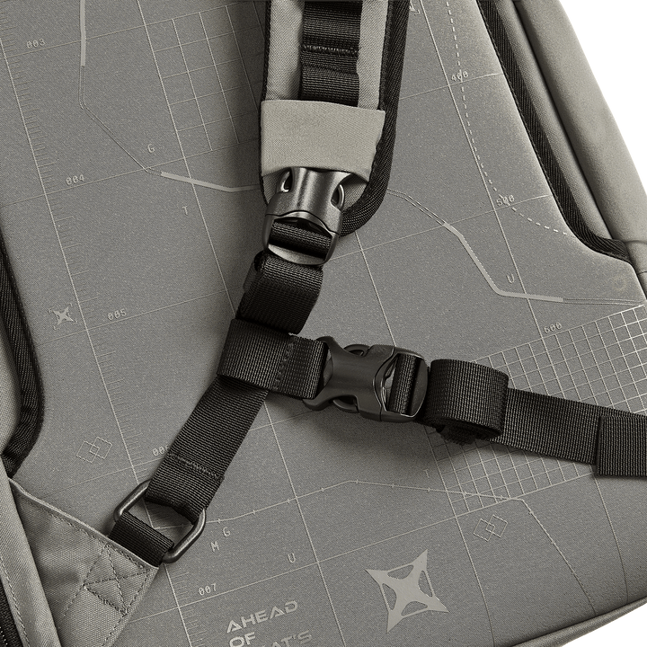 Close-up of the Vertx Gamut 22L Sling by Vertx, a gray, travel-friendly backpack with black adjustable straps, a plastic buckle, and fabric featuring white geometric patterns and the text "AHEAD OF WHAT’S POSSIBLE.