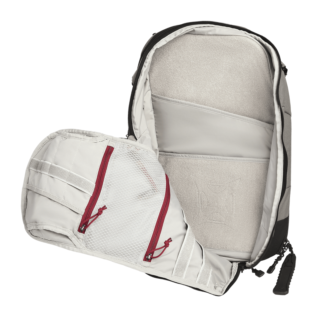 The Vertx Gamut 22L Sling by Vertx is a travel-friendly backpack shown open, revealing two mesh zippered pockets with red zippers on the flap and padded compartments—including a dedicated CCW compartment—inside the main section.