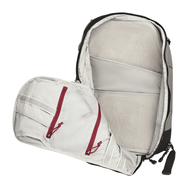 The Vertx Gamut 22L Sling by Vertx is a travel-friendly backpack shown open, revealing two mesh zippered pockets with red zippers on the flap and padded compartments—including a dedicated CCW compartment—inside the main section.