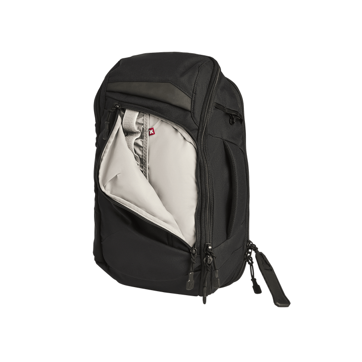 The Vertx Gamut 18L Sling by Vertx is a black backpack featuring a large front zipper pocket, partially open to reveal a light gray interior lining, inner sleeve, and rapid access CCW compartment. The bag stands upright on a white background.