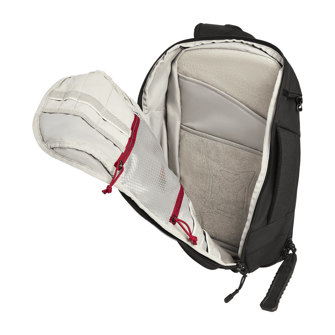 The Vertx Gamut 18L Sling by Vertx is shown open, displaying a padded compartment, beige interior lining, and two mesh zippered pockets with red pulls on the inside of the flap for quick access.
