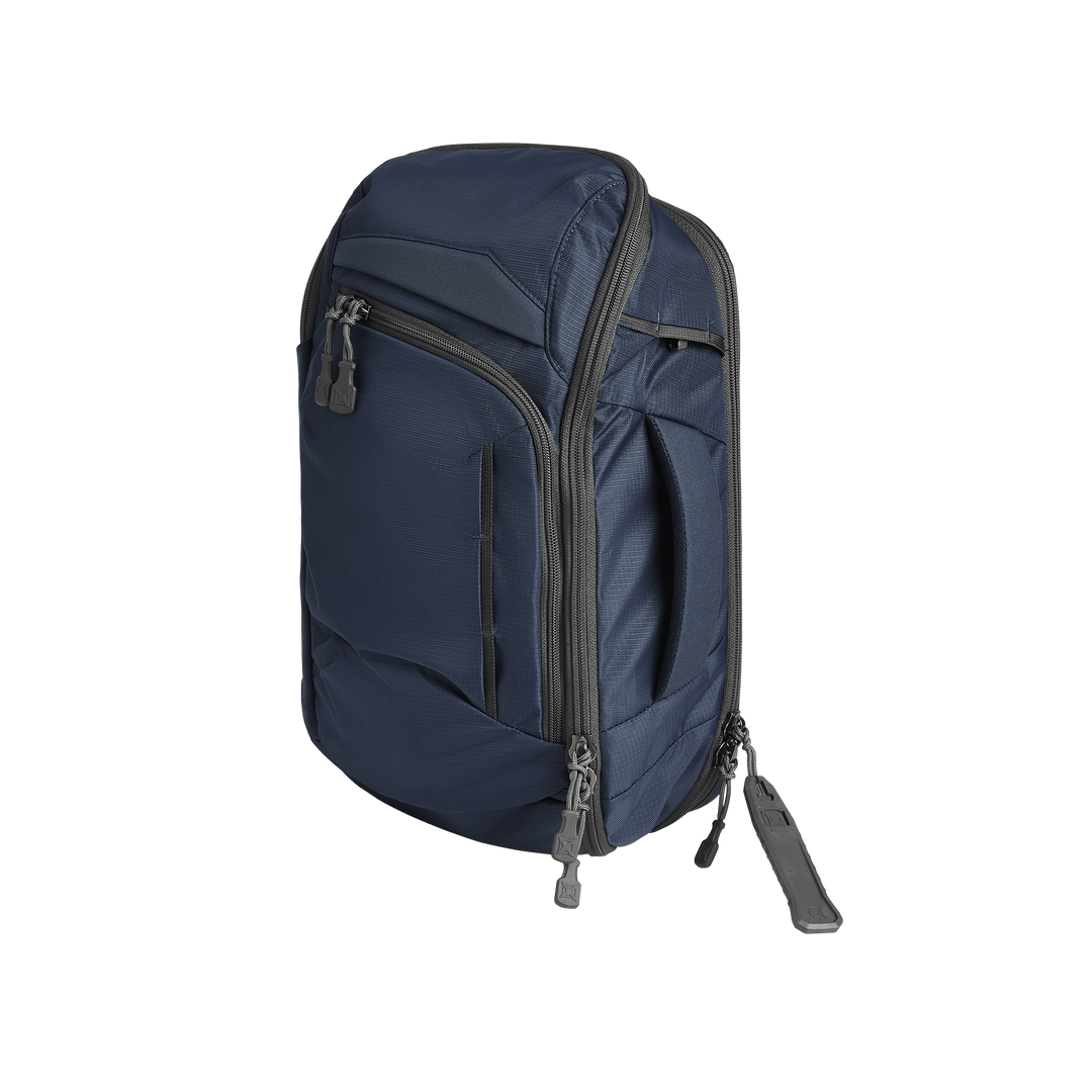 The Vertx Gamut 18L Sling by Vertx, a navy blue compact backpack with multiple zippered compartments and gray zipper pulls, stands upright against a plain white background.