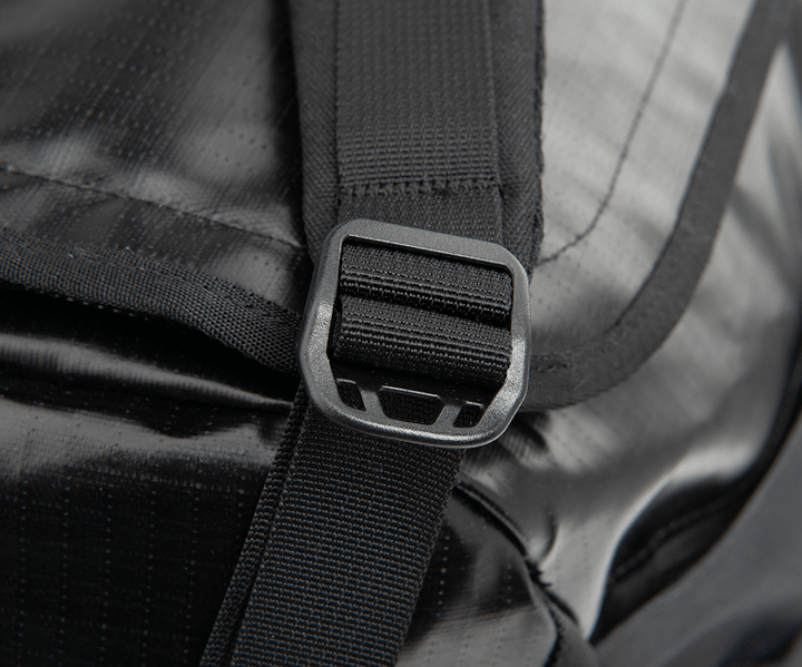 A close-up showcases the black strap with a rectangular, rounded-edge buckle on the lustrous Vertx RLT Duffel backpack. The strap is securely threaded through the buckle, highlighting its customizable storage options and the slick, durable appearance of this Vertx product.