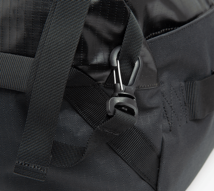 The close-up highlights the robust design of the Vertx RLT Duffel, emphasizing its strap and secure buckle. The image showcases the textured material of this black bag, which is renowned for offering customizable storage options.