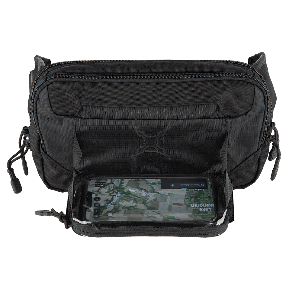 A black Vertx SOCP Tactical Fanny Pack, open to reveal a transparent pocket holding a smartphone displaying a map. The Vertx bag, featuring multiple zippers, is crafted to securely hold various items and can even accommodate a body armor insert for added protection.