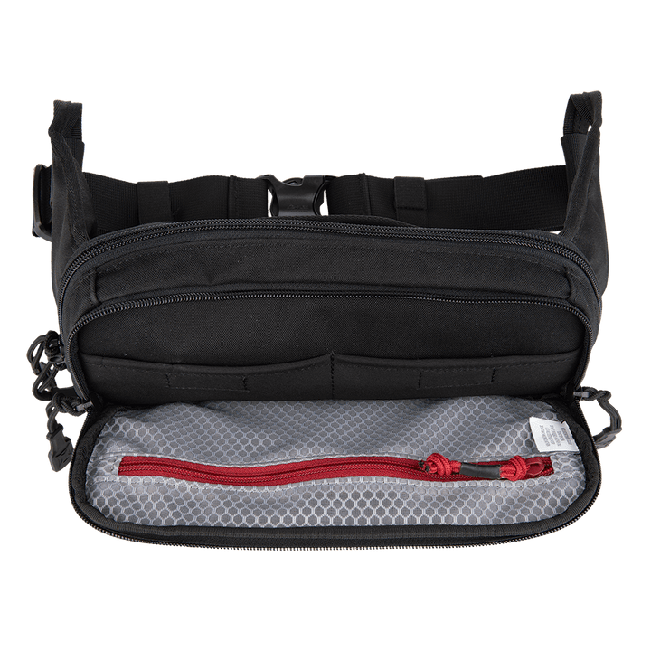 A Vertx SOCP Tactical Fanny Pack in black, its front compartment unzipped to reveal a gray mesh pocket with a red zipper. The pack features multiple straps and buckles on the exterior, designed to hold additional gear or even a small body armor insert.