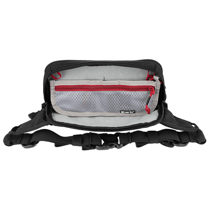 A black Vertx SOCP Tactical Fanny Pack from Vertx, with its top compartment open, displays an interior lined with light gray fabric. Inside, there's a mesh zippered pocket accented with red trim. The bag features multiple external straps, buckles, padded areas, and space for a body armor insert.