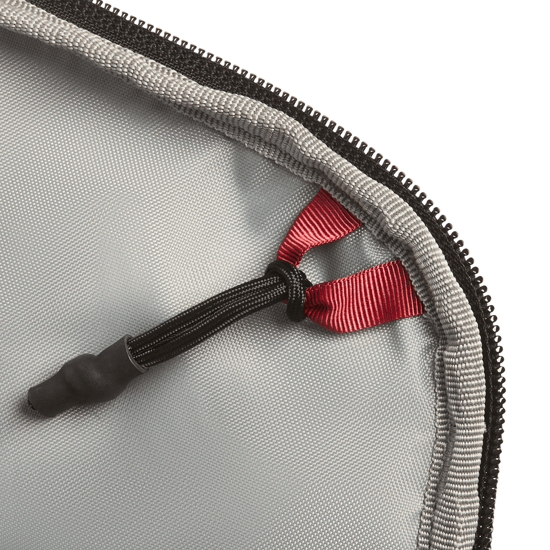 Close-up of the Vertx Everyday Fanny Pack 2.1 in gray, featuring a black zipper and a red ribbon loop attached to a black elastic cord with a rubber end, secured at the corner of the ballistic-panel compatible case.