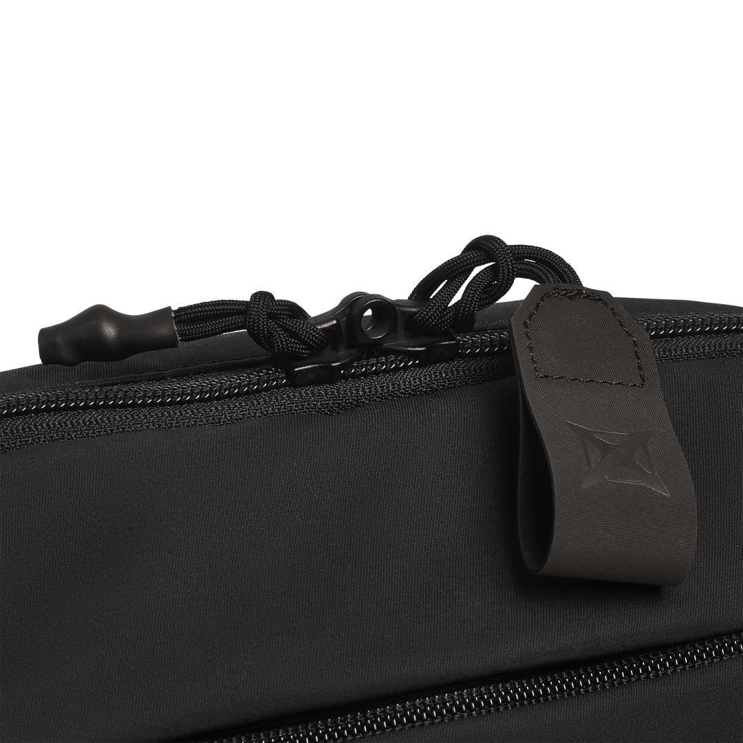 Close-up of the Vertx Everyday Fanny Pack 2.1 in black, featuring a smooth material, a zipper with a fabric pull tab and black corded pull, and an embossed Vertx logo on the tab.