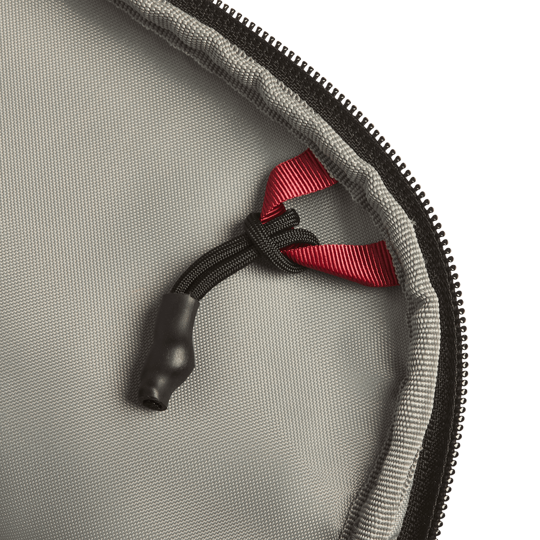 Close-up of the Vertx Everyday Fanny Pack+ by Vertx, showing gray fabric, a black zipper, a black cord with a plastic end, and a red ribbon loop—designed to be compatible with ballistic panels for extra protection.