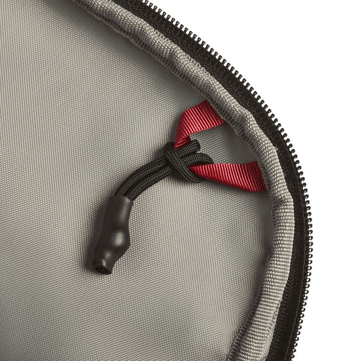Close-up of the Vertx Everyday Fanny Pack+ by Vertx, showing gray fabric, a black zipper, a black cord with a plastic end, and a red ribbon loop—designed to be compatible with ballistic panels for extra protection.