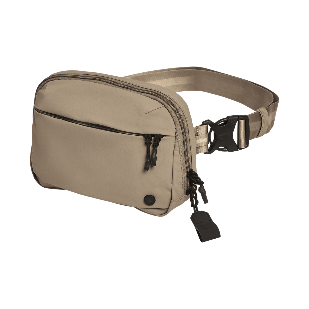 The Vertx Everyday Fanny Pack+ by Vertx is a beige crossbody bag with a front zip pocket, black zipper pulls, adjustable strap, and plastic buckle. Ballistic panel compatible, it's shown against a plain white background.