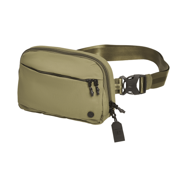 A Vertx Everyday Fanny Pack+ in olive green, featuring a front zip pocket, double zipper closure, an adjustable strap with black buckle and tag, and CCW ballistic-panel compatibility, is shown on a white background.