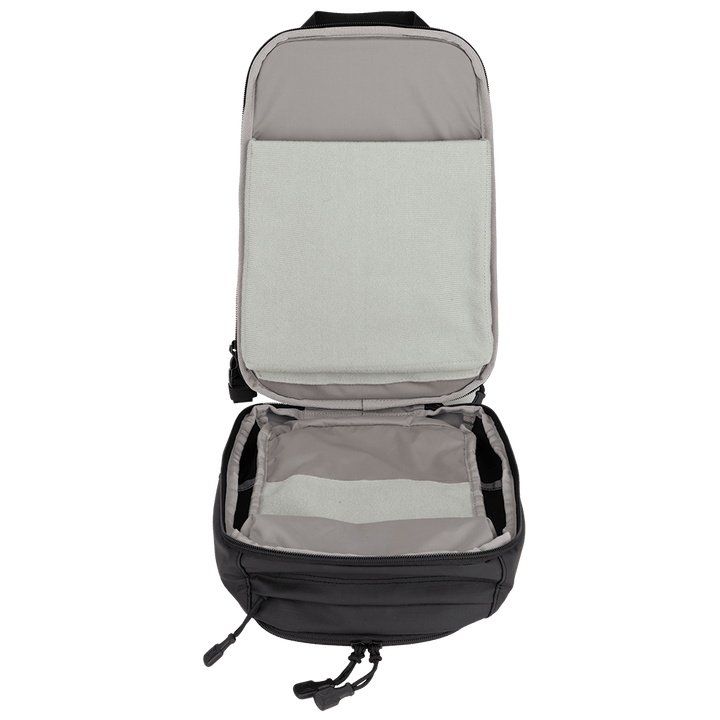 The Vertx Urban Ghost Sling, in black and gray, is laid flat with its compartments visible. The top flap is open, showcasing a padded section along with a spacious main compartment perfect for everyday carry gear. The bag is empty inside.