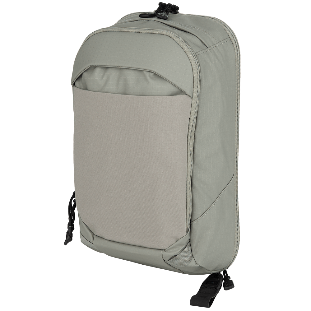 The Vertx Urban Ghost Sling, a gray backpack from Vertx, is on display showcasing a minimalist design. It includes a spacious main compartment, a smaller front pocket, and adjustable straps. Perfect for everyday use, it has a smooth texture with a subtle grid pattern on the material.