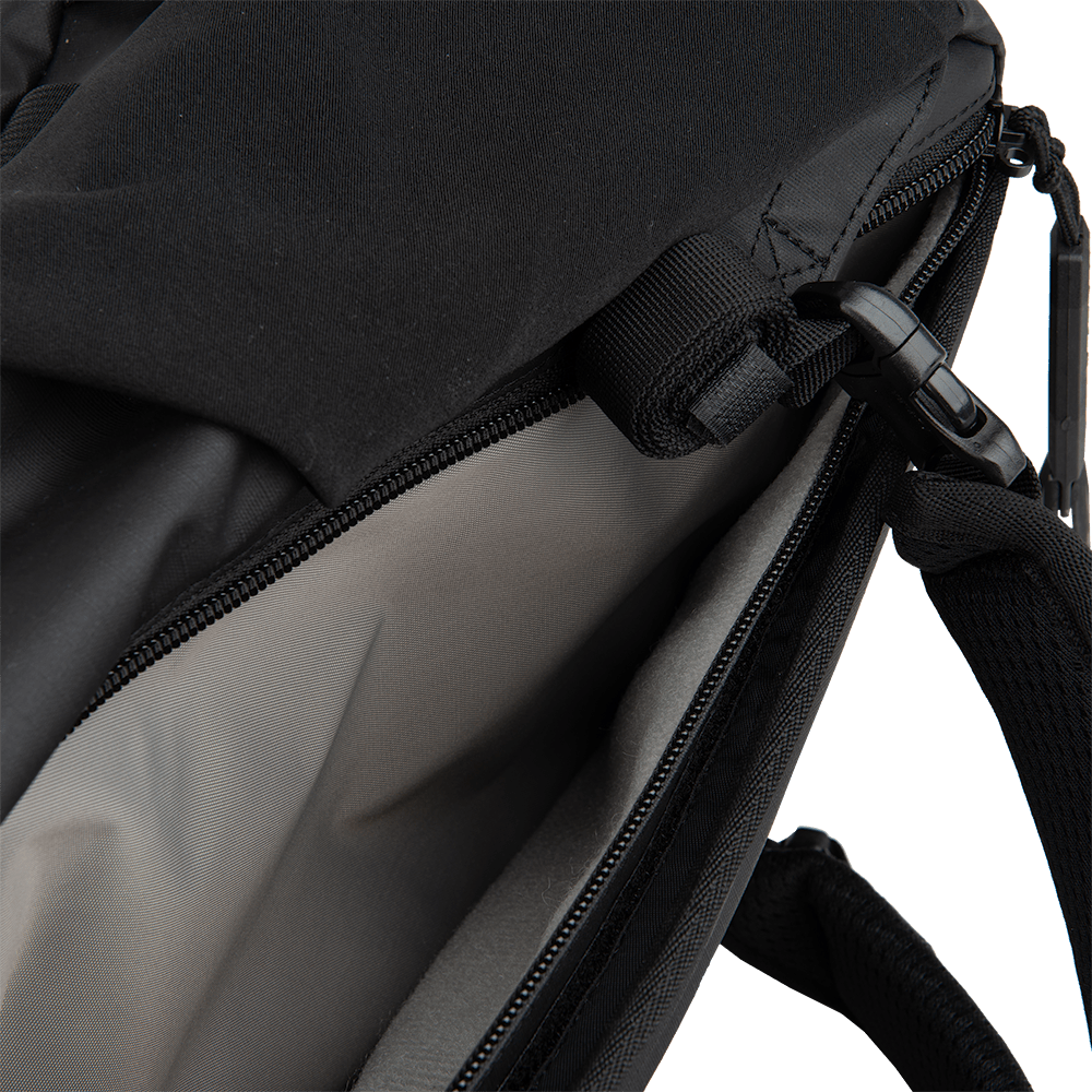 A close-up image of an open Vertx Urban Ghost Pack. The partially open zipper reveals the light gray interior lining, crafted from durable ripstop fabric. A black strap is visible on the right side, partially hanging from the pack.