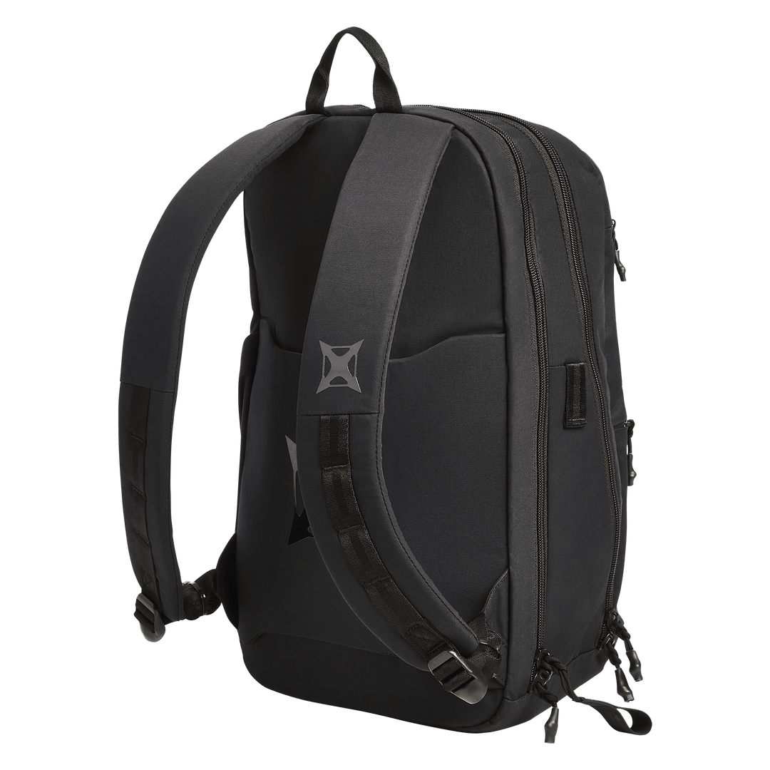 The Vertx Any Day Backpack by Vertx is a black EDC pack with padded shoulder straps, a top carry handle, zippered compartments, a small geometric logo on the left strap, and a ballistic-panel compatible design. Shown photographed on a white background.