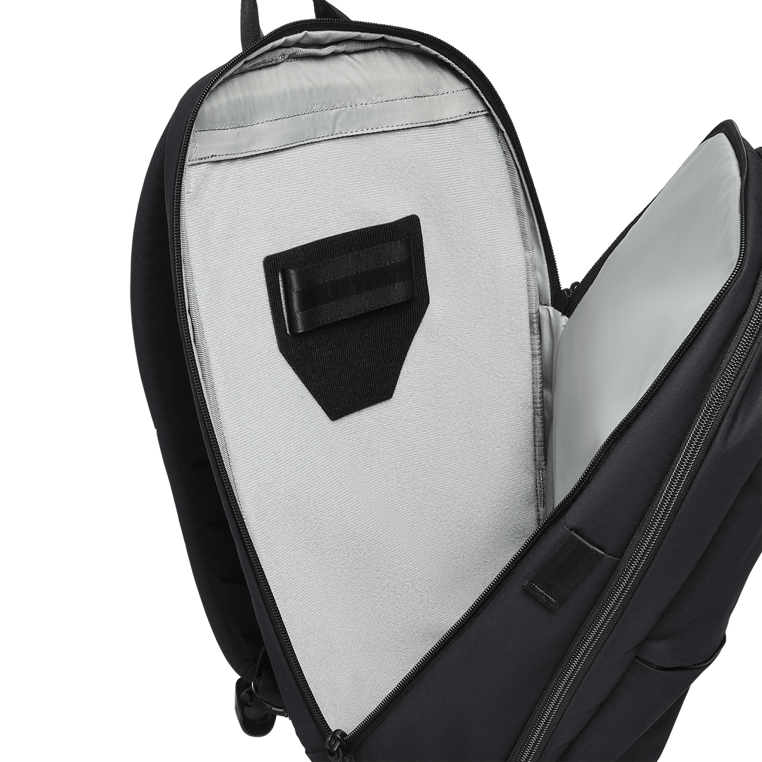 A close-up of a partially unzipped Vertx Any Day Backpack by Vertx shows its light gray interior, black Velcro strap, and a padded compartment compatible with ballistic panels.
