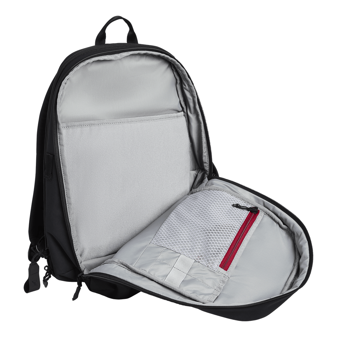 The Vertx Any Day Backpack by Vertx is shown unzipped, revealing a light gray interior with an open laptop sleeve and a mesh zippered pocket with a red zipper inside the front flap.