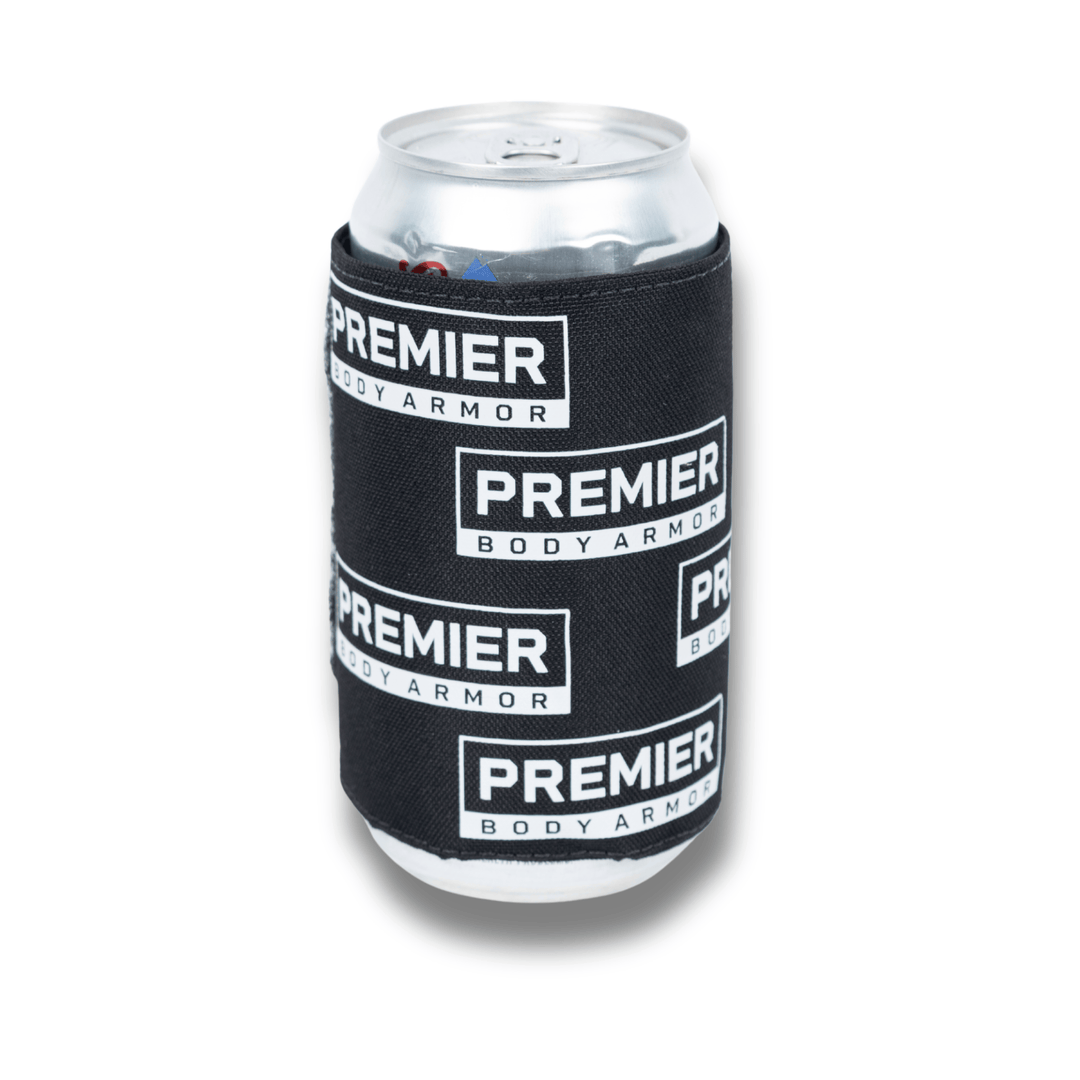 A silver soda can sits in the Premier Body Armor Bulletproof Can Cooler – Limited Edition, a black sleeve with multiple white "Premier Body Armor" logos repeated across its surface, set against a bright white background.