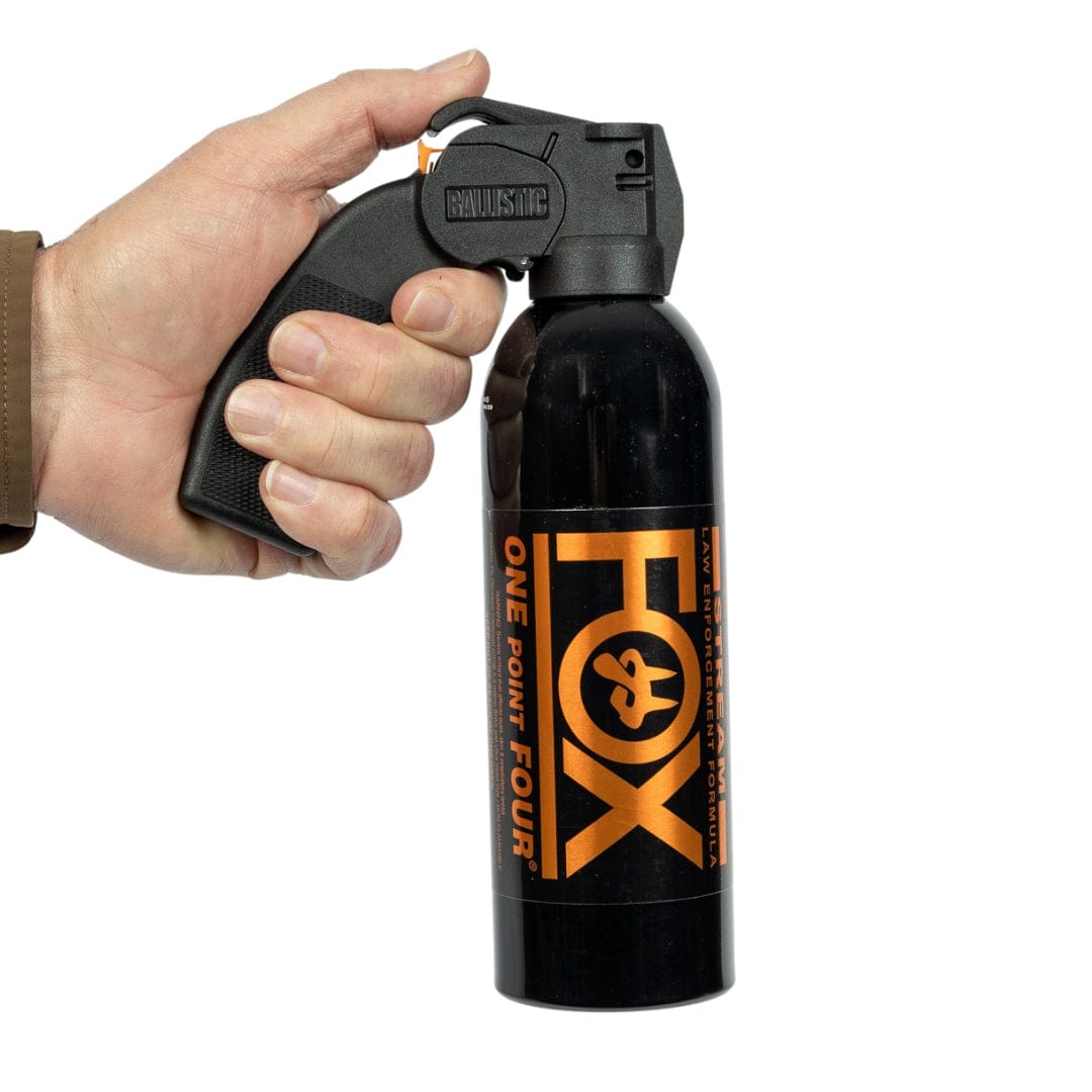 A hand holds a Fox Labs One Point Four 16oz Pistol Grip Pepper Spray canister, featuring an orange and black label; this police-strength self-defense spray is made by Fox Labs.