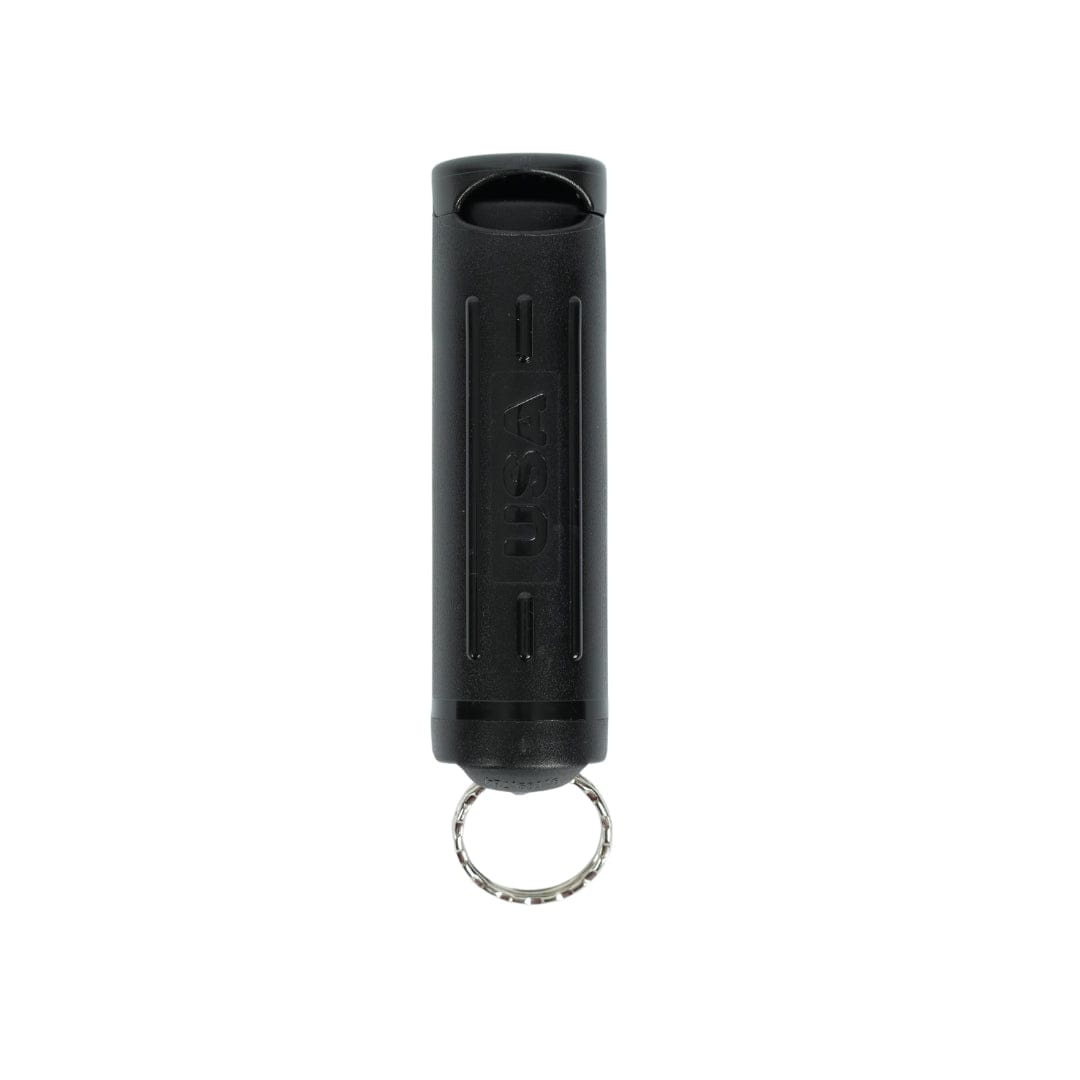 The Fox Labs Personal Pocket Unit by Fox Labs is a black cylindrical keychain pepper spray with a metallic key ring at the bottom. "USA" is embossed vertically on the front, making it an ideal personal defense accessory. Plain white background.