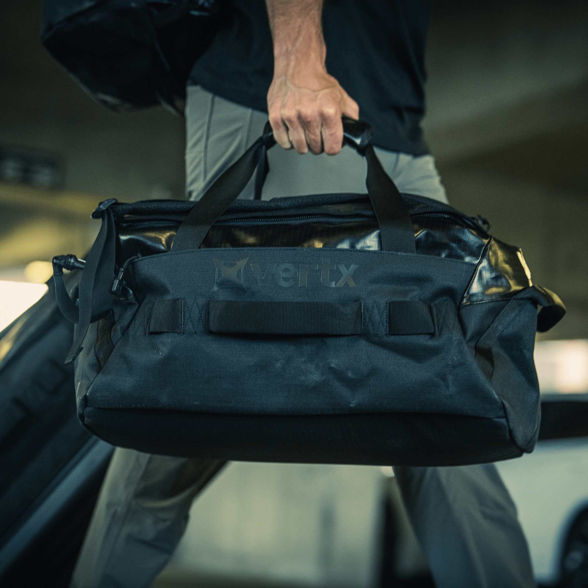 The Vertx RLT Duffel bag, displayed against a white background, offers robust construction with various compartments, strong handles, and an adjustable shoulder strap. It comes with reinforced material, subtle branding, and customizable storage options for optimal convenience.