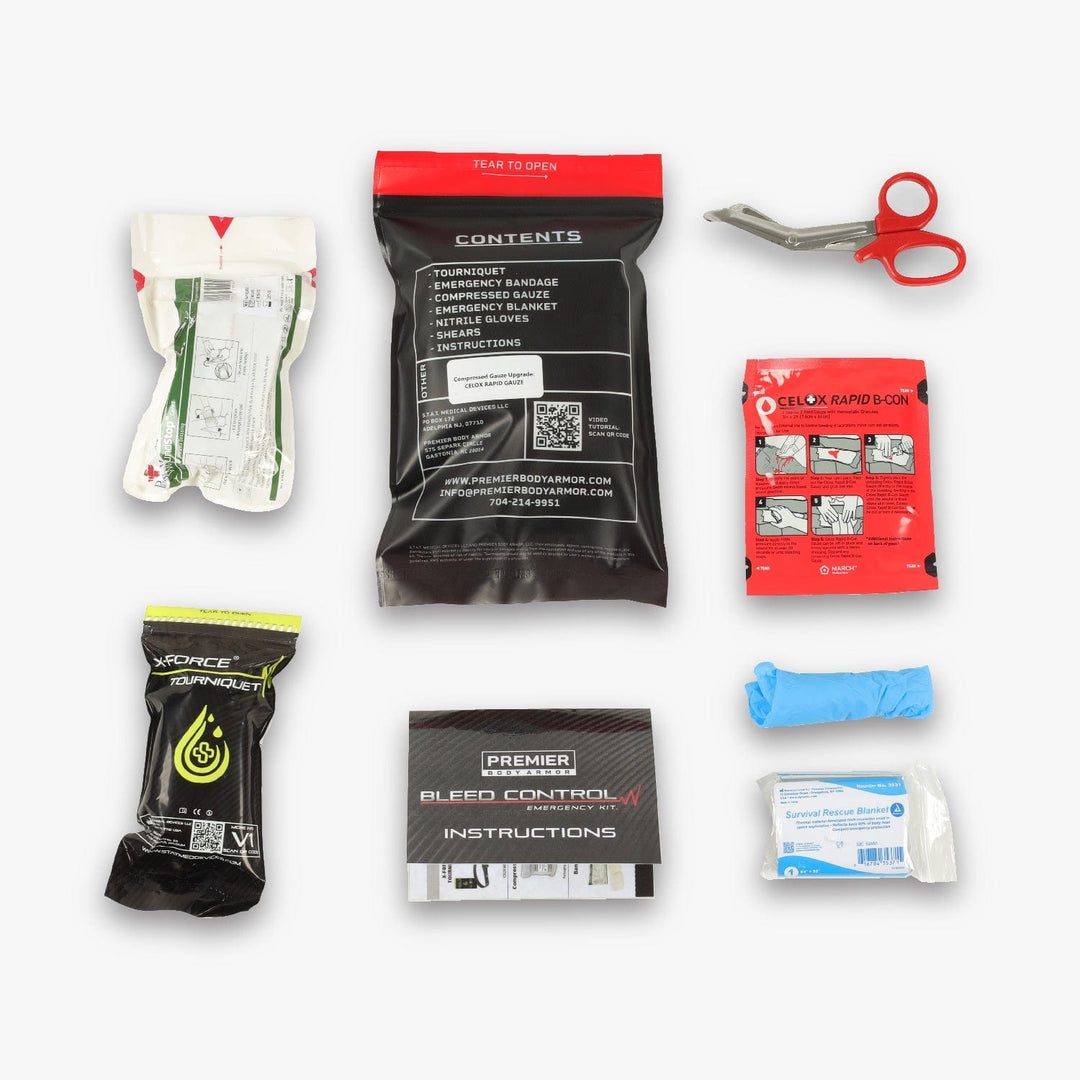 A flat lay of the PBA Bleed Control Kit contents including a pair of medical scissors, a compressed bandage, an S.T.A.T. Tourniquet, gauze, adhesive bandages, a pair of medical gloves, bleed control instructions from STAT's PBA Bleed Control Kit, and a red rapid box labeled "Celox.